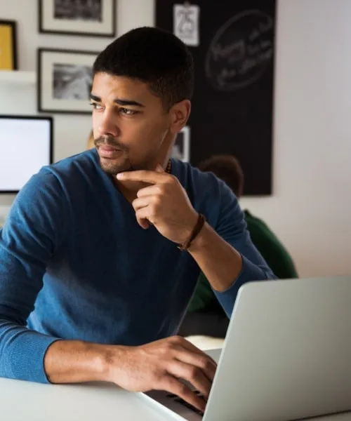 A man sat at a desk, using a laptop with a thoughtful expression.