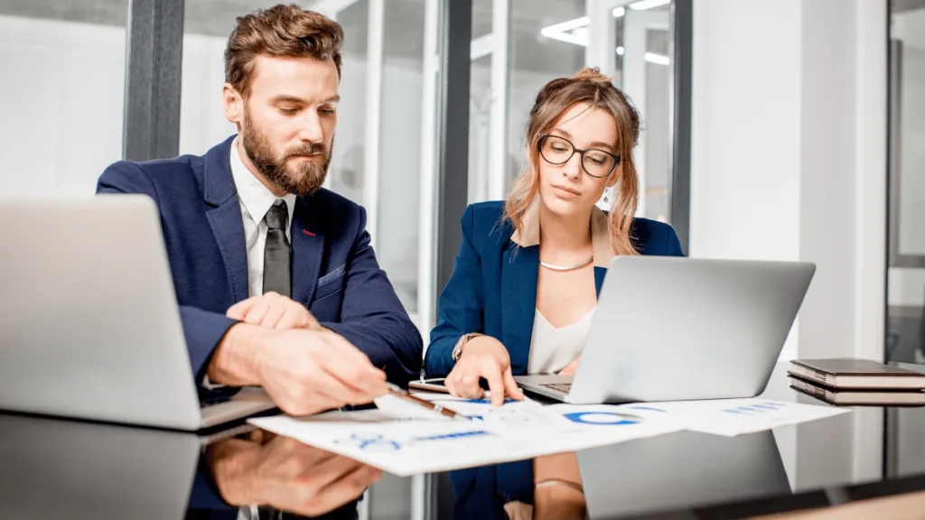 A man and a woman sitting at an office table looking at analytic data - Equinox Consulting
